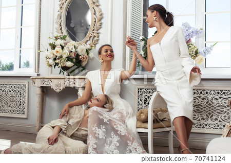 three young pretty lady in white lace fashion style dress posing in rich interior of royal hotel room, luxury lifestyle people concept, bride on wedding day three young pretty lady in white lace fashion style dress posing in rich interior of royal hotel room, luxury lifestyle people concept, bride on wedding day 70741124