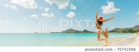 Christmas fun travel vacation bikini girl jumping of joy on Caribbean beach santa hat woman happy panoramic banner landscape holiday Christmas fun travel vacation bikini girl jumping of joy on Caribbean beach santa hat woman happy panoramic banner landscape holiday 70742898