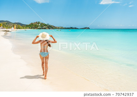 Beach travel vacation woman walking on luxury Caribbean cruise destination Antigua island in bikini wearing beach hat, carefree on holidays on Jolly Beach. Girl on travel vacation holidays swim model 70742937