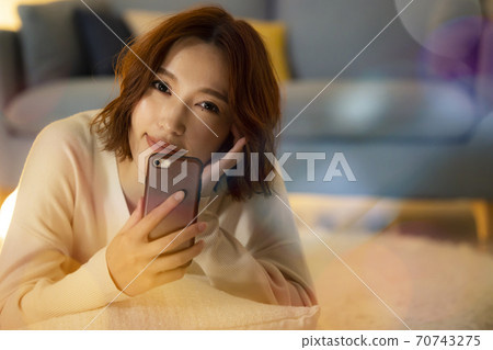 A woman looking at a smartphone in the living room at night A woman looking at a smartphone in the living room at night 70743275