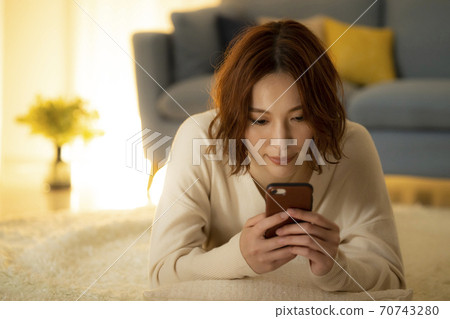 A woman looking at a smartphone in the living room at night A woman looking at a smartphone in the living room at night 70743280