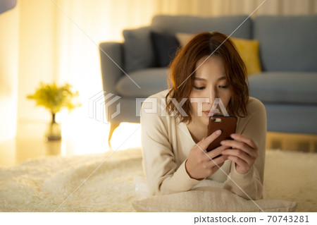 A woman looking at a smartphone in the living room at night A woman looking at a smartphone in the living room at night 70743281