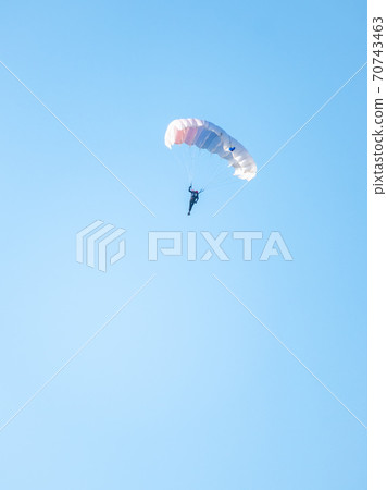 one parachutist floats slowly at low altitude on the background of clear sky 70743463