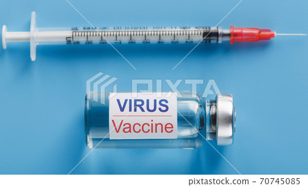 An ampoule with a vaccine on the label of the ampoule, a syringe for viruses and diseases on a blue background. Free space on the ampoule for text. For isolation of the vertical frames An ampoule with a vaccine on the label of the ampoule, a syringe for viruses and diseases on a blue background. Free space on the ampoule for text. For isolation of the vertical frames 70745085
