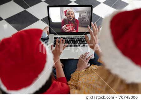 Woman and daughter in Santa hats having a video chat with another woman on laptop at home 70748000