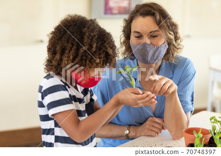 Boy wearing face mask holding plant in class 70748397