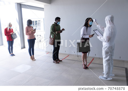 Health worker wearing protective clothes checking temperature of businesswoman 70748878