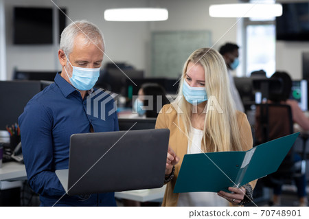 Senior businessman and businesswoman wearing face masks working together at modern office 70748901