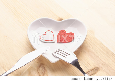 Red heart on a white plate in the form of a heart on a wooden background with a fork and knife. Festive background to the Valentine's Day and Mother's Day Red heart on a white plate in the form of a heart on a wooden background with a fork and knife. Festive background to the Valentine's Day and Mother's Day 70751142