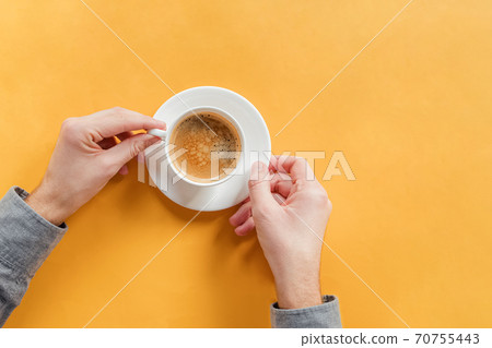 Man's hands holding a cup of coffee on yellow table Man's hands holding a cup of coffee on yellow table 70755443
