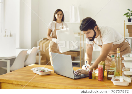 Young workers of food delivery company placing online orders and packing boxed orders Young workers of food delivery company placing online orders and packing boxed orders 70757972