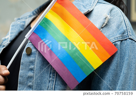 Asian lady wearing blue jean jacket or denim shirt and holding rainbow color flag, symbol of LGBT pride month celebrate annual in June social of gay, lesbian, bisexual, transgender, human rights. Asian lady wearing blue jean jacket or denim shirt and holding rainbow color flag, symbol of LGBT pride month celebrate annual in June social of gay, lesbian, bisexual, transgender, human rights. 70758159