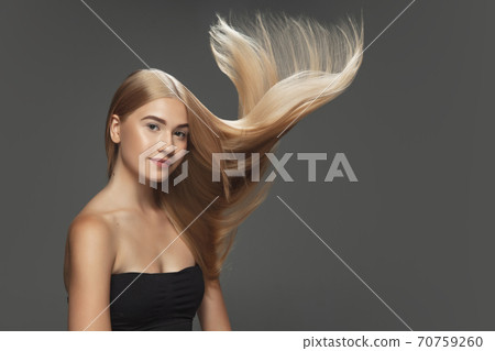 Beautiful model with long smooth, flying blonde hair isolated on dark studio background. 70759260