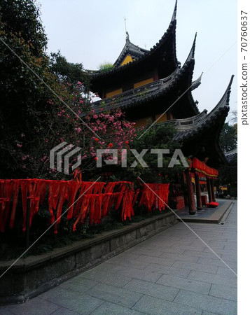 A pink flower basin in front of a Buddhist temple in China with a sharp roof and a prayer belt made of red cloth 70760637