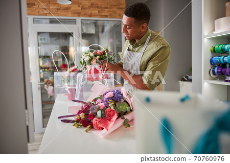 Florist moving a pot of roses into a carrier bag 70760976