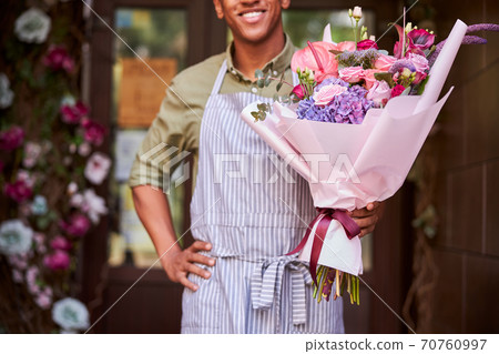 Nice flower shop worker demonstrating wrapped flowers 70760997