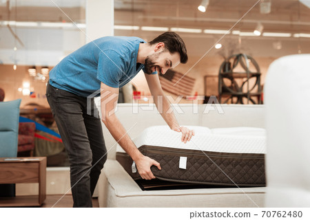 A man in a furniture store is testing a mattress. A man in a furniture store is testing a mattress. 70762480
