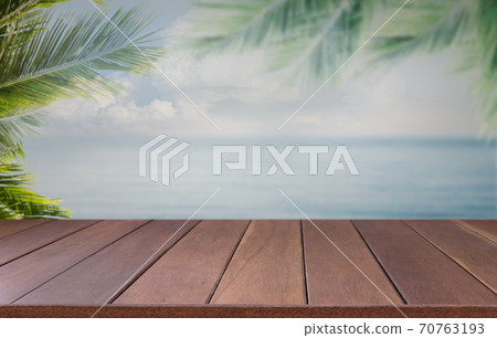 Brown wooden planks with blur beach sea sky on background and  palm leaves on foreground,summer concepts Brown wooden planks with blur beach sea sky on background and  palm leaves on foreground,summer concepts 70763193