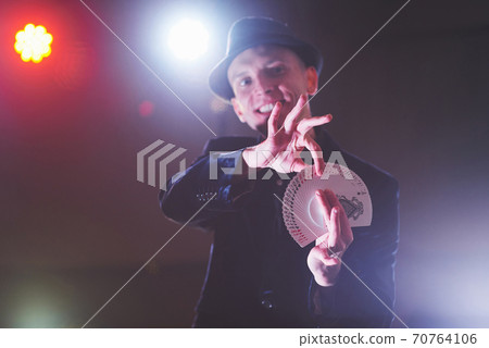 Magician showing trick with playing cards. Magic or dexterity, circus, gambling. Prestidigitator in dark room with fog 70764106