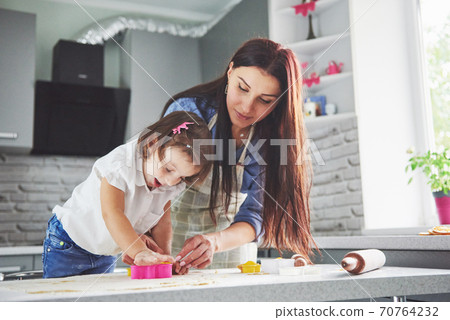 Happy family in the kitchen. Holiday food concept. Mother and daughter preparing the dough, bake cookies. Happy family in making cookies at home. Homemade food and little helper Happy family in the kitchen. Holiday food concept. Mother and daughter preparing the dough, bake cookies. Happy family in making cookies at home. Homemade food and little helper 70764232