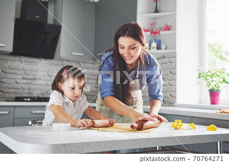Happy family in the kitchen. Holiday food concept. Mother and daughter preparing the dough, bake cookies. Happy family in making cookies at home. Homemade food and little helper 70764271