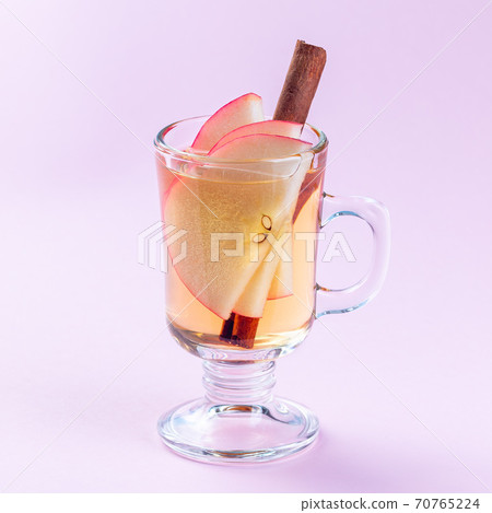 Glass of white glogg or mulled wine with apple slices and cinnamon stick on pink background, square Glass of white glogg or mulled wine with apple slices and cinnamon stick on pink background, square 70765224