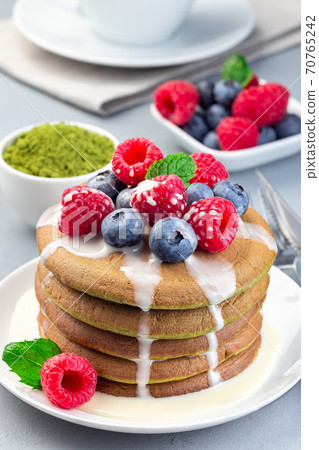Matcha pancakes served with condensed milk, blueberry and raspberry on white plate, vertical 70765242
