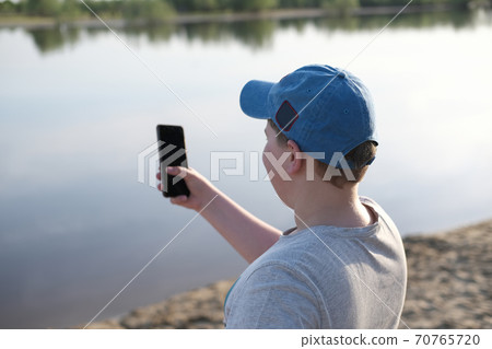 stout teenager boy making selfie. boy standing near the river and looking at smartphone 70765720