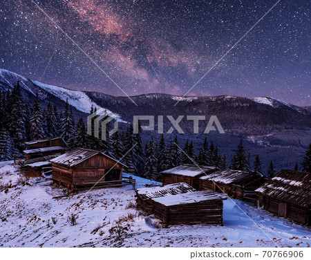 magical winter snow covered trees and mountain village. Winter landscape. Vibrant night sky with stars and nebula and galaxy. 70766906