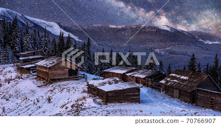 magical winter snow covered trees and mountain village. Winter landscape. Vibrant night sky with stars and nebula and galaxy. 70766907