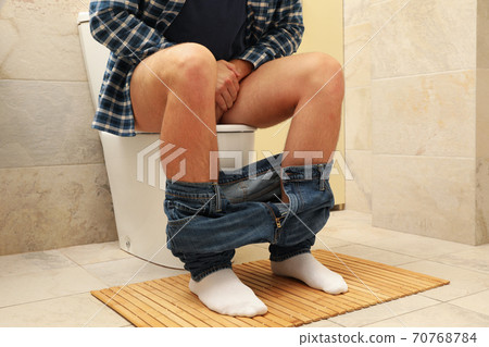 A man sits with his pants down on the toilet 70768784