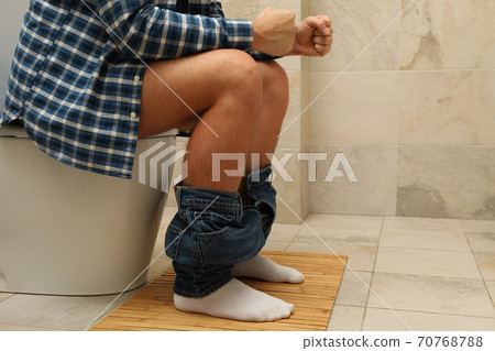 A man sits with his pants down on the toilet 70768788