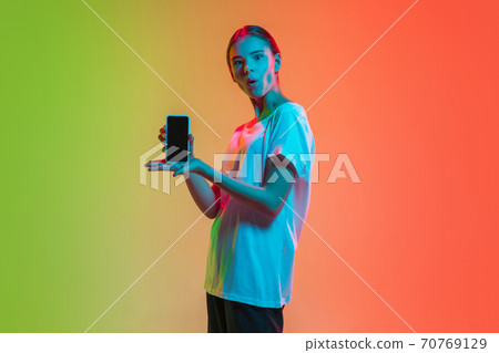Young caucasian girl's portrait on gradient green-orange studio background in neon light 70769129