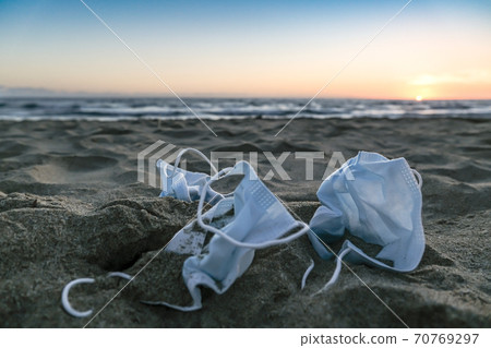 Medical face masks discarded on beach over sunset background,covid19 pandemic disease pollution  70769297