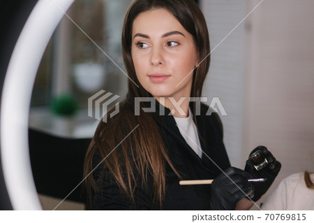 Portrait of professional female brow master in black robe with black gloves use brush and henna for eyebrows 70769815