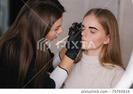 Brow master applies henna on eyebrows for beautiful blond hair woman Brow master applies henna on eyebrows for beautiful blond hair woman 70769816
