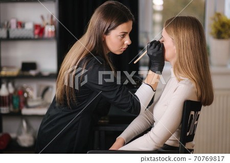 Brow master applies henna on eyebrows for beautiful blond hair woman Brow master applies henna on eyebrows for beautiful blond hair woman 70769817