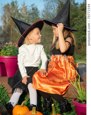 Sisters in witch costumes looking at each other outdoors Sisters in witch costumes looking at each other outdoors 70771594