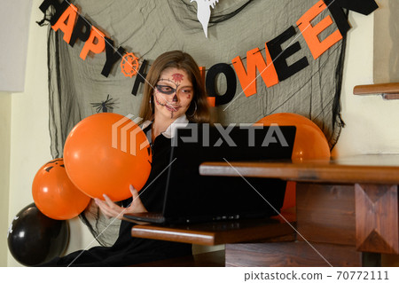 A girl in a Halloween make-up congratulates her friends and family on Halloween with a video call via a laptop A girl in a Halloween make-up congratulates her friends and family on Halloween with a video call via a laptop 70772111