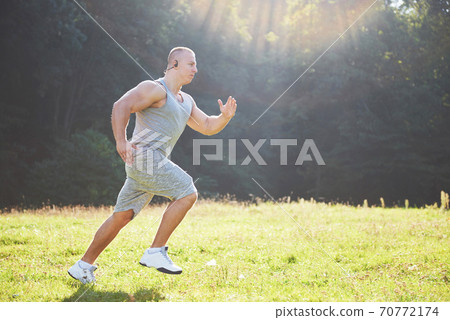 Fitness man athlete jogging in the nature during sunset. Person running working out living an active lifestyle training cardio in summer in sportswear and shoes. Fitness man athlete jogging in the nature during sunset. Person running working out living an active lifestyle training cardio in summer in sportswear and shoes. 70772174