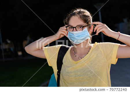 Young woman with glasses put on a protective mask. Coronavirus devices and life with new normal and social distancing Young woman with glasses put on a protective mask. Coronavirus devices and life with new normal and social distancing 70772240
