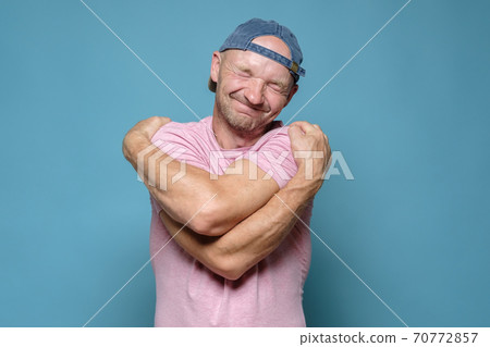 If you are lonely, hug yourself. Cute man in a cap and a pink T-shirt hugs himself and dreams with If you are lonely, hug yourself. Cute man in a cap and a pink T-shirt hugs himself and dreams with 70772857