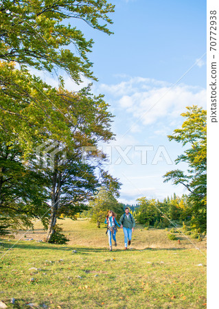 Beautiful couple walking with backpacks on the green meadow, while traveling high in the mountains during the summer time. Rear view 70772938