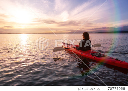 Sea Kayaking in calm waters during a colorful and vibrant sunset. Sea Kayaking in calm waters during a colorful and vibrant sunset. 70773066