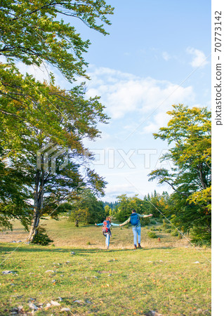 Beautiful couple walking with backpacks on the green meadow, while traveling high in the mountains during the summer time. Rear view 70773142