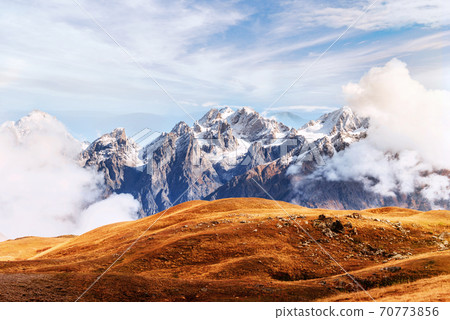 Autumn landscape and snow mountains in beautiful cumulus clouds. Main Caucasian Ridge. Type Mount Ushba Mheyer, Georgia Autumn landscape and snow mountains in beautiful cumulus clouds. Main Caucasian Ridge. Type Mount Ushba Mheyer, Georgia 70773856