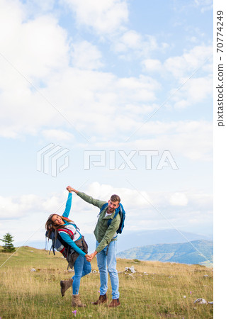 Happy travelers couple conquered top of mountain, raises hands up Happy travelers couple conquered top of mountain, raises hands up 70774249