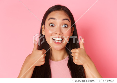 Beauty, fashion and lifestyle concept. Close-up of enthusiastic good-looking asian girl like idea, praising great choice, looking amazed and surprised showing thumbs-up in approval, pink wall Beauty, fashion and lifestyle concept. Close-up of enthusiastic good-looking asian girl like idea, praising great choice, looking amazed and surprised showing thumbs-up in approval, pink wall 70774608