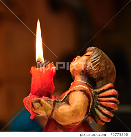 Wooden angel with a burning candle in his arms. Wooden angel with a burning candle in his arms. 70775296