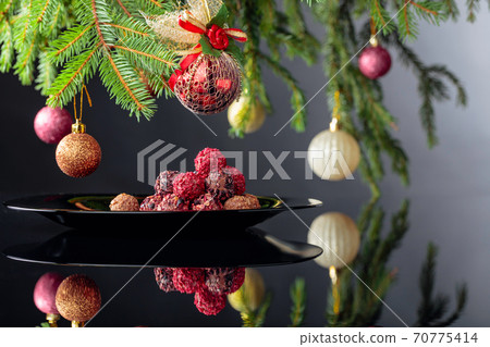 Chocolate truffles on a black plate and Christmas tree. Chocolate truffles on a black plate and Christmas tree. 70775414